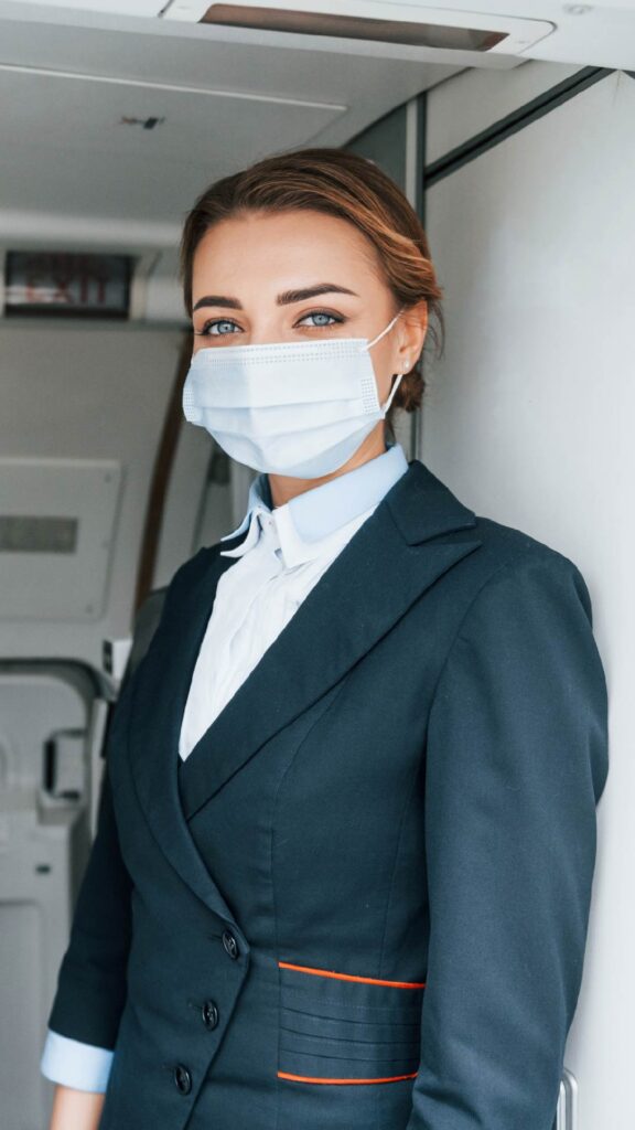 Flight attendant wearing mask in an airplane looking at us